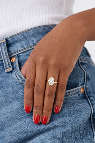 Hand wearing a gold ring with a diamond on a blue denim background