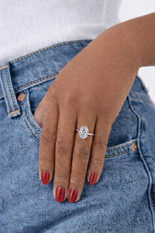Hand wearing a diamond ring with blue jeans and a white shirt in the background